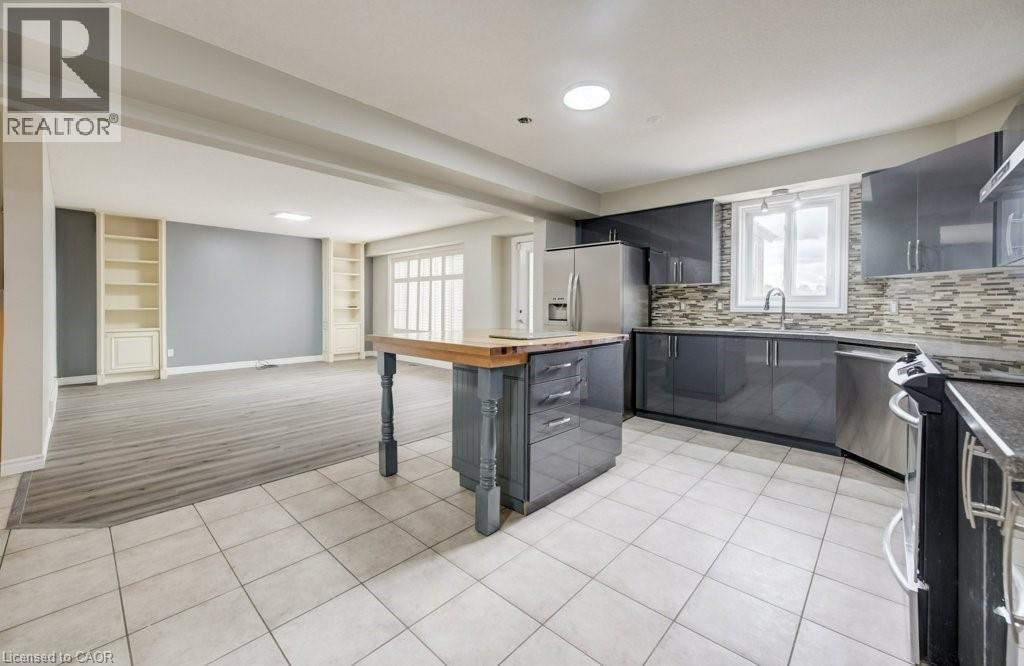 Open-concept kitchen and living area featuring high-gloss gray cabinetry, stainless steel appliances, a center island with wood-finish countertop, and tile flooring - 123 Forest Edge Trail, Kitchener, ON - Indoor Photo Showing Kitchen