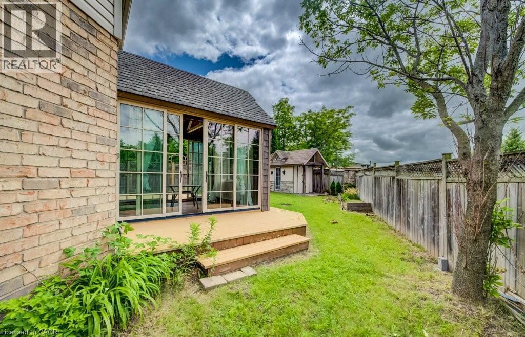 Rear exterior featuring a sunroom with multiple glass panels, an attached wooden deck with steps, a detached shed, a wooden privacy fence, and mature trees - 123 Forest Edge Trail, Kitchener, ON - Outdoor