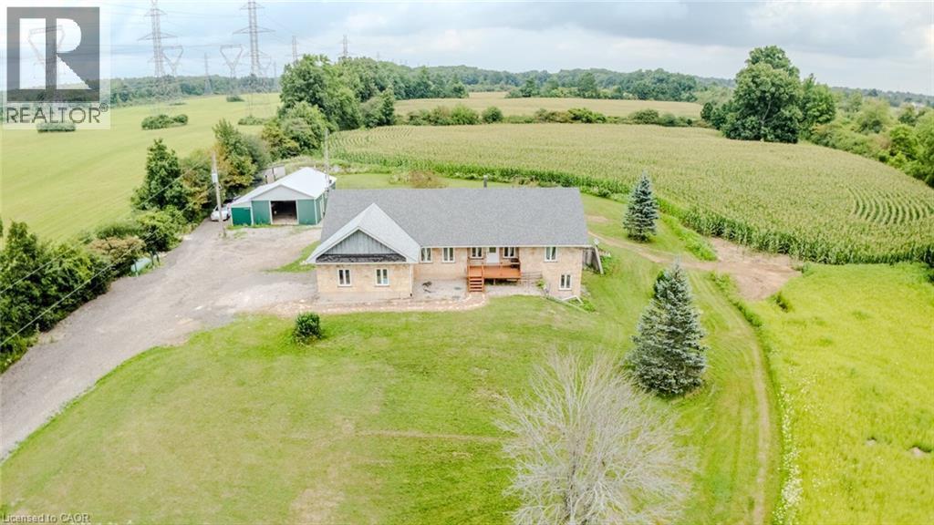 Stone exterior property with a shingled roof, featuring a wooden deck, mature evergreen trees, and an expansive lawn - 107 6Th Line Line, Caledonia, ON - Outdoor With View