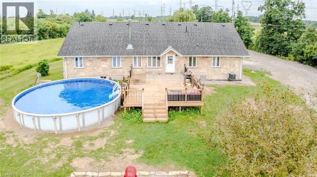 Stone exterior with a dark shingle roof, accompanied by a wooden deck and an oval above-ground pool - 107 6Th Line Line, Caledonia, ON - Outdoor With Above Ground Pool