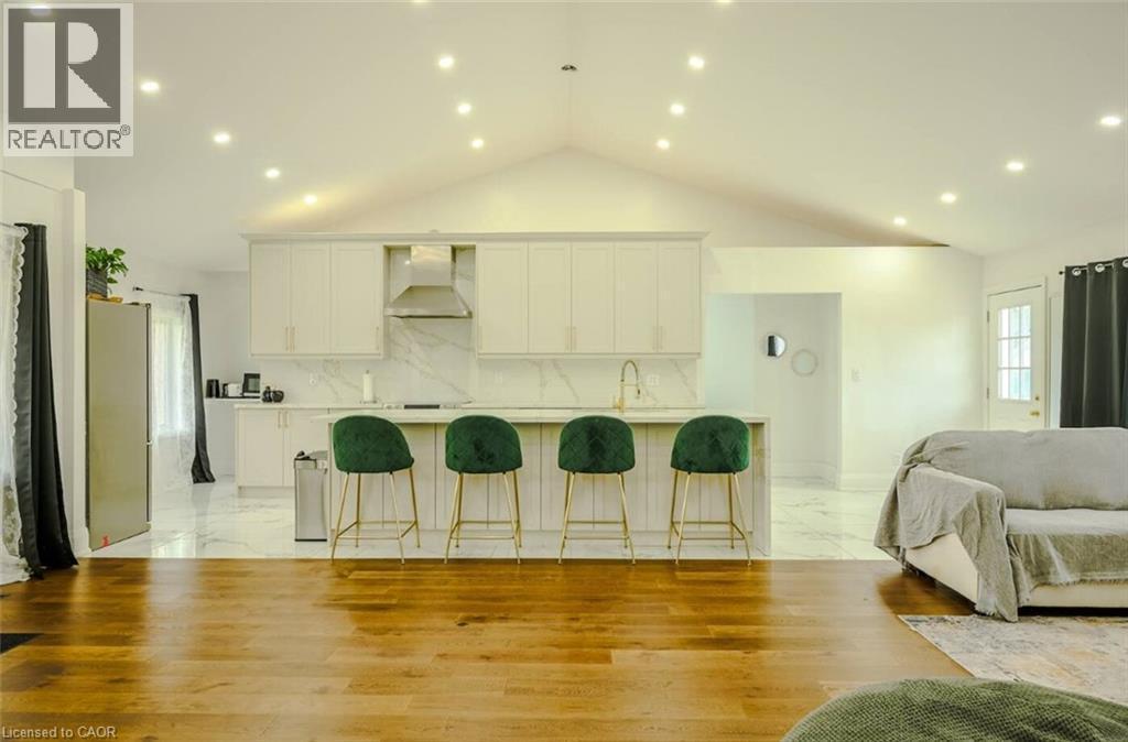 Vaulted ceiling with recessed lighting, wood-finish flooring, kitchen island with built-in cabinetry, stainless steel range hood, and marble-finish backsplash - 107 6Th Line Line, Caledonia, ON - Indoor Photo Showing Living Room