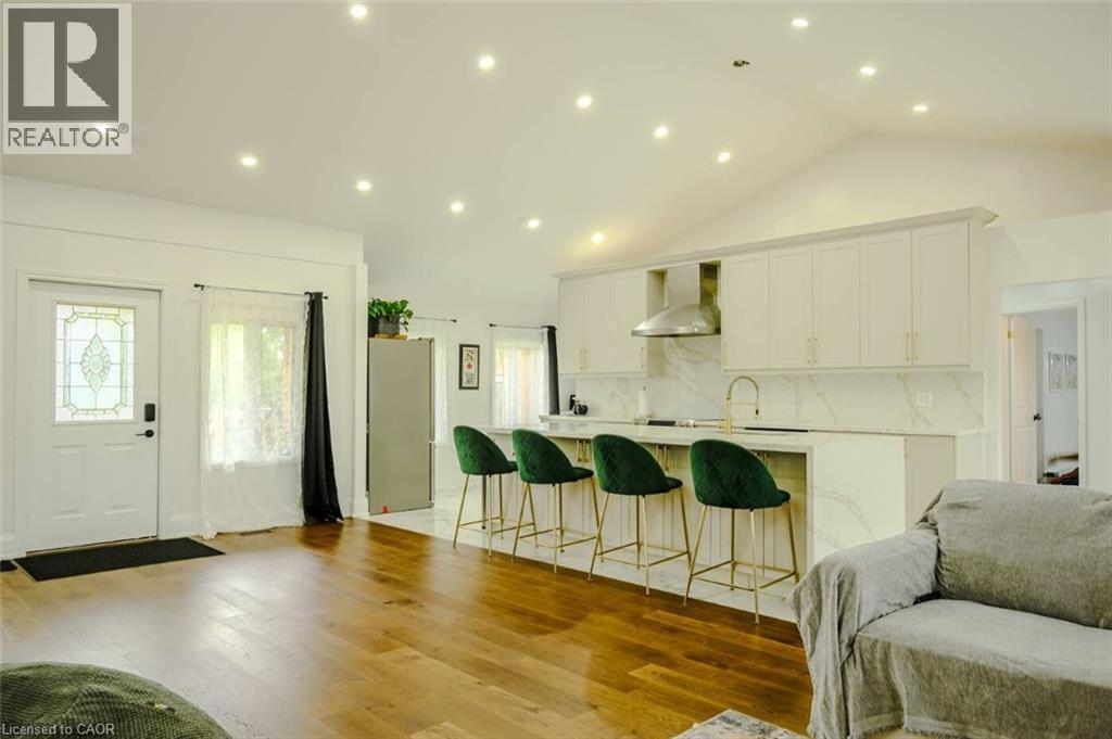 Spacious interior with wood-finish flooring, vaulted ceilings, recessed lighting, and a kitchen featuring a large island with white cabinetry and a stainless steel range hood - 107 6Th Line Line, Caledonia, ON - Indoor