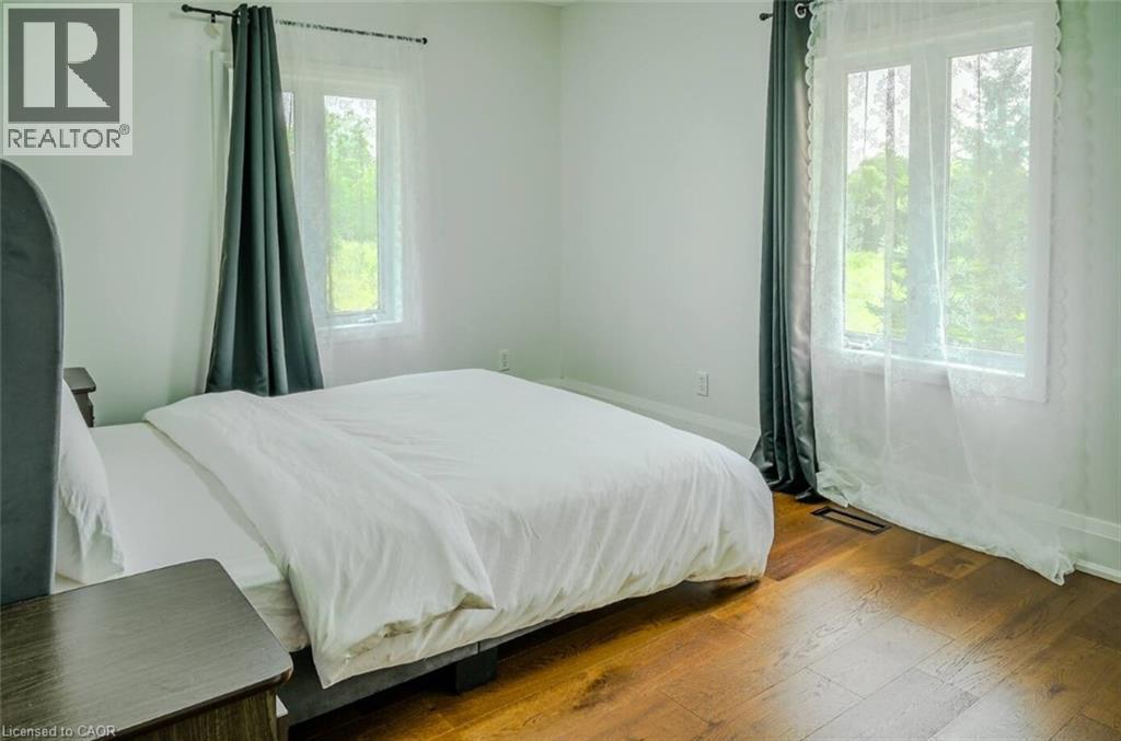Hardwood flooring throughout, featuring two large windows with white trim, and white wall finishes - 107 6Th Line Line, Caledonia, ON - Indoor Photo Showing Bedroom