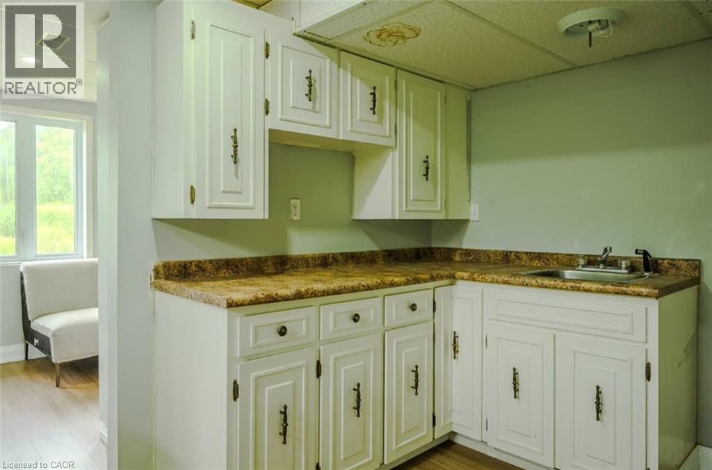 White cabinetry with dark hardware, L-shaped countertop, stainless steel sink, and wood-finish flooring - 107 6Th Line Line, Caledonia, ON - Indoor