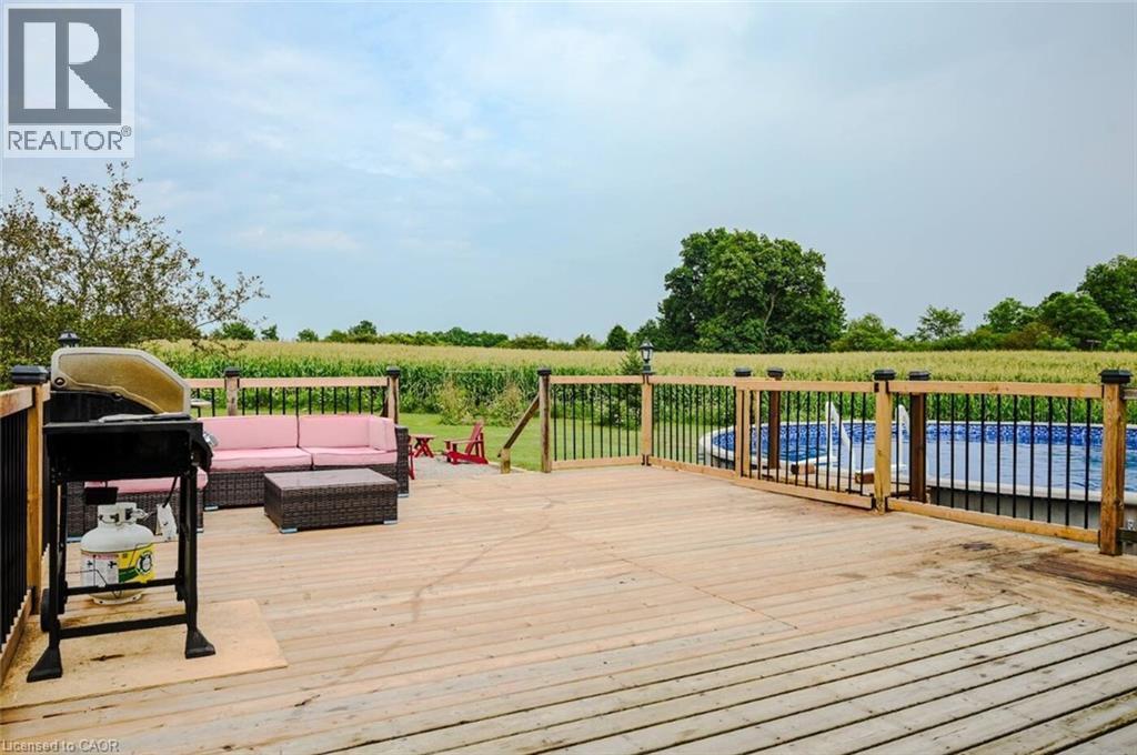 Expansive wood-finish deck with a black metal and wood railing system, featuring an above-ground pool with a blue liner - 107 6Th Line Line, Caledonia, ON - Outdoor With Above Ground Pool