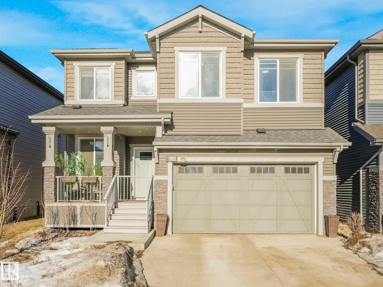 Two-story home with a prominent front entrance, featuring a covered porch with stone-clad pillars and a white railing - 8641 Mayday Wynd Sw, Edmonton, AB - Outdoor