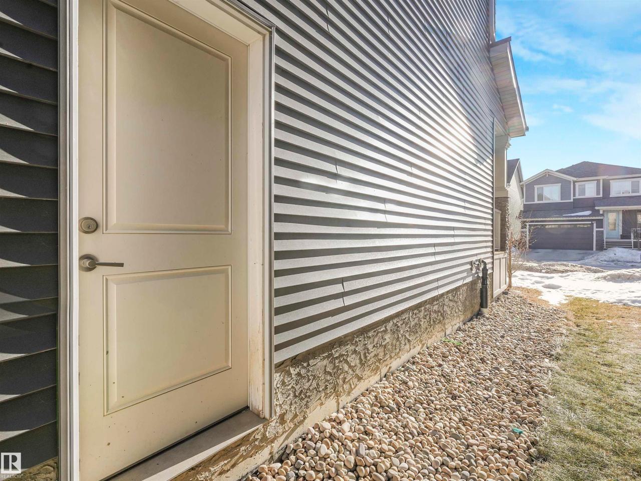 Cream-paneled exterior door with brushed nickel hardware, set against two-tone siding - 8641 Mayday Wynd Sw, Edmonton, AB - Outdoor With Exterior