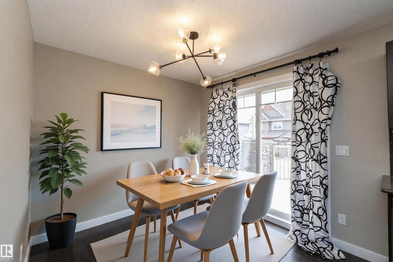 Dining area featuring a modern linear chandelier, dark wood-finish flooring, and a sliding glass door - 117 Callaghan Drive Sw, Edmonton, AB - Indoor Photo Showing Dining Room