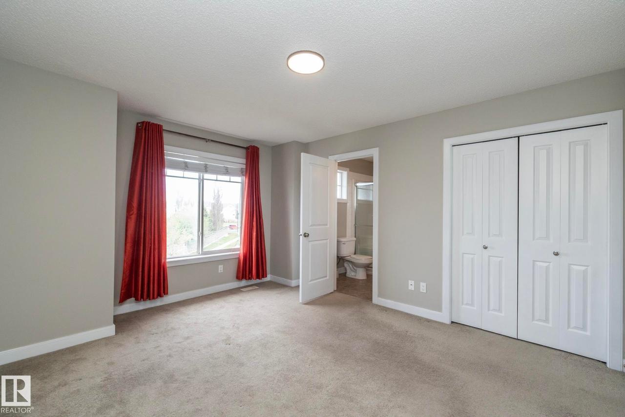 Carpeted room featuring a double window, overhead flush-mount lighting, bi-fold closet doors, and light grey wall paint with white baseboards - 117 Callaghan Drive Sw, Edmonton, AB - Indoor