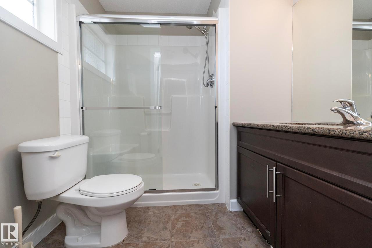 Bathroom featuring a glass-enclosed shower, dark wood-finish vanity with a stone countertop, chrome fixtures, and neutral wall tones - 117 Callaghan Drive Sw, Edmonton, AB - Indoor Photo Showing Bathroom
