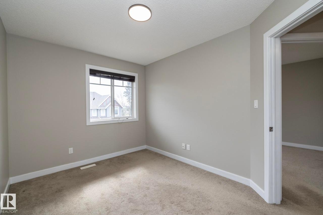 Neutral toned walls and carpeting, featuring a window with dark blinds and a single ceiling light fixture - 117 Callaghan Drive Sw, Edmonton, AB - Indoor Photo Showing Other Room