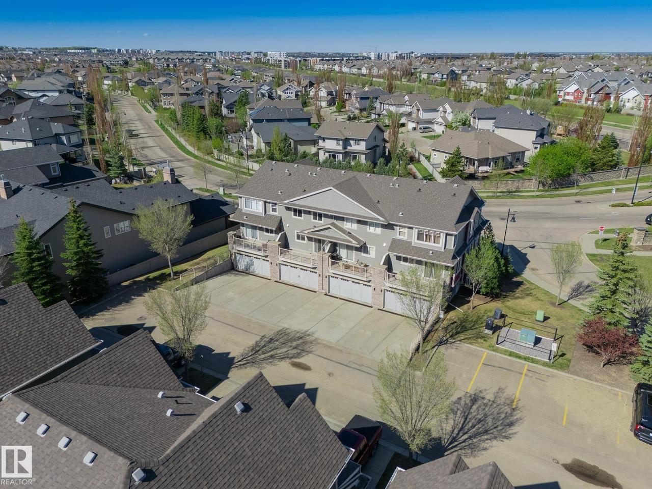 Multi-level residential building featuring private balconies, individual garage doors, and a paved parking area - 117 Callaghan Drive Sw, Edmonton, AB - Outdoor With View