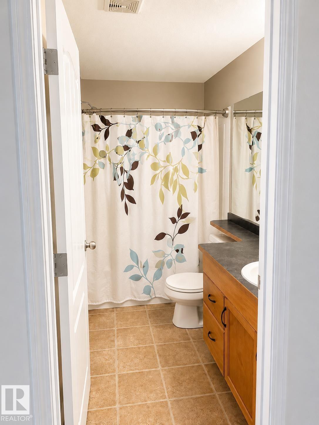 Bathroom featuring a wood-finish vanity with dark countertop, white porcelain sink, and ceramic tile flooring - #115 5340 199 St Nw, Edmonton, AB - Indoor Photo Showing Bathroom