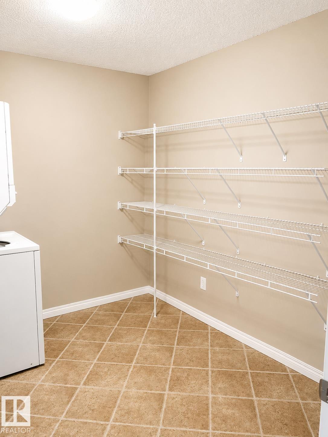 Utility room featuring extensive wire shelving, a tiled floor, and a neutral wall palette - #115 5340 199 St Nw, Edmonton, AB - Indoor With Storage