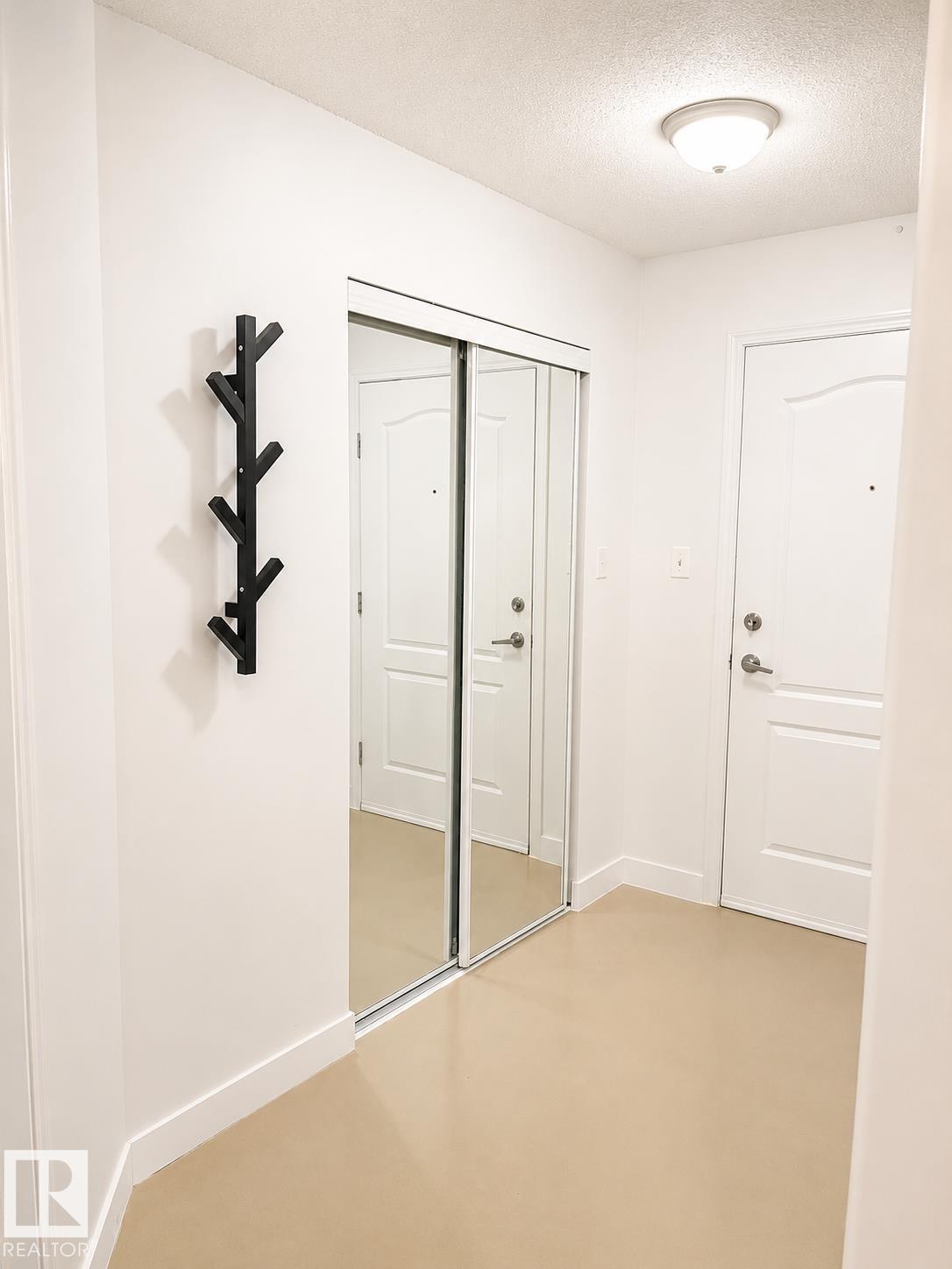Entryway featuring a full-height mirrored closet with sliding doors, a flush-mount ceiling light fixture, and light-toned flooring - #115 5340 199 St Nw, Edmonton, AB - Indoor Photo Showing Other Room