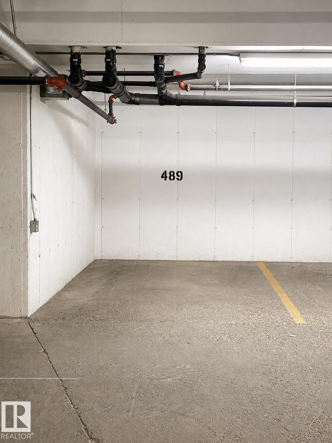 Designated parking space featuring concrete flooring, numbered demarcation, and overhead utility lines - #115 5340 199 St Nw, Edmonton, AB - Indoor Photo Showing Garage