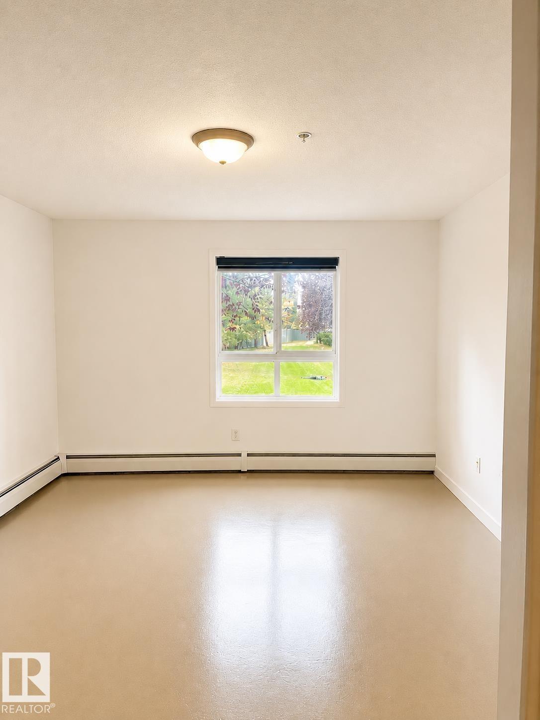 Bright interior space featuring a window with exterior views, light-toned flooring, white walls, and a ceiling-mounted light fixture - #115 5340 199 St Nw, Edmonton, AB - Indoor Photo Showing Other Room