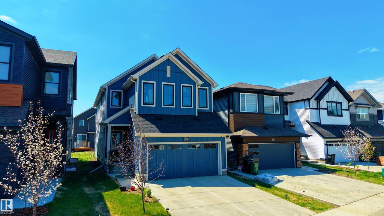 Modern two-story home featuring a blue siding exterior, a two-car attached garage, and a concrete driveway - 2120 Muckleplum Crescent Sw, Edmonton, AB - Outdoor With Facade