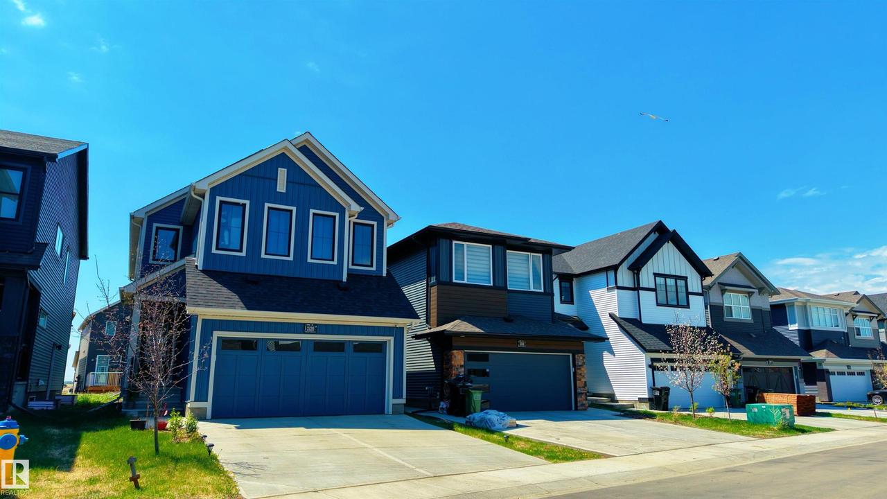 Contemporary two-story residence featuring blue siding, white trim, a dark shingle roof, and an attached two-car garage - 2120 Muckleplum Crescent Sw, Edmonton, AB - Outdoor With Facade