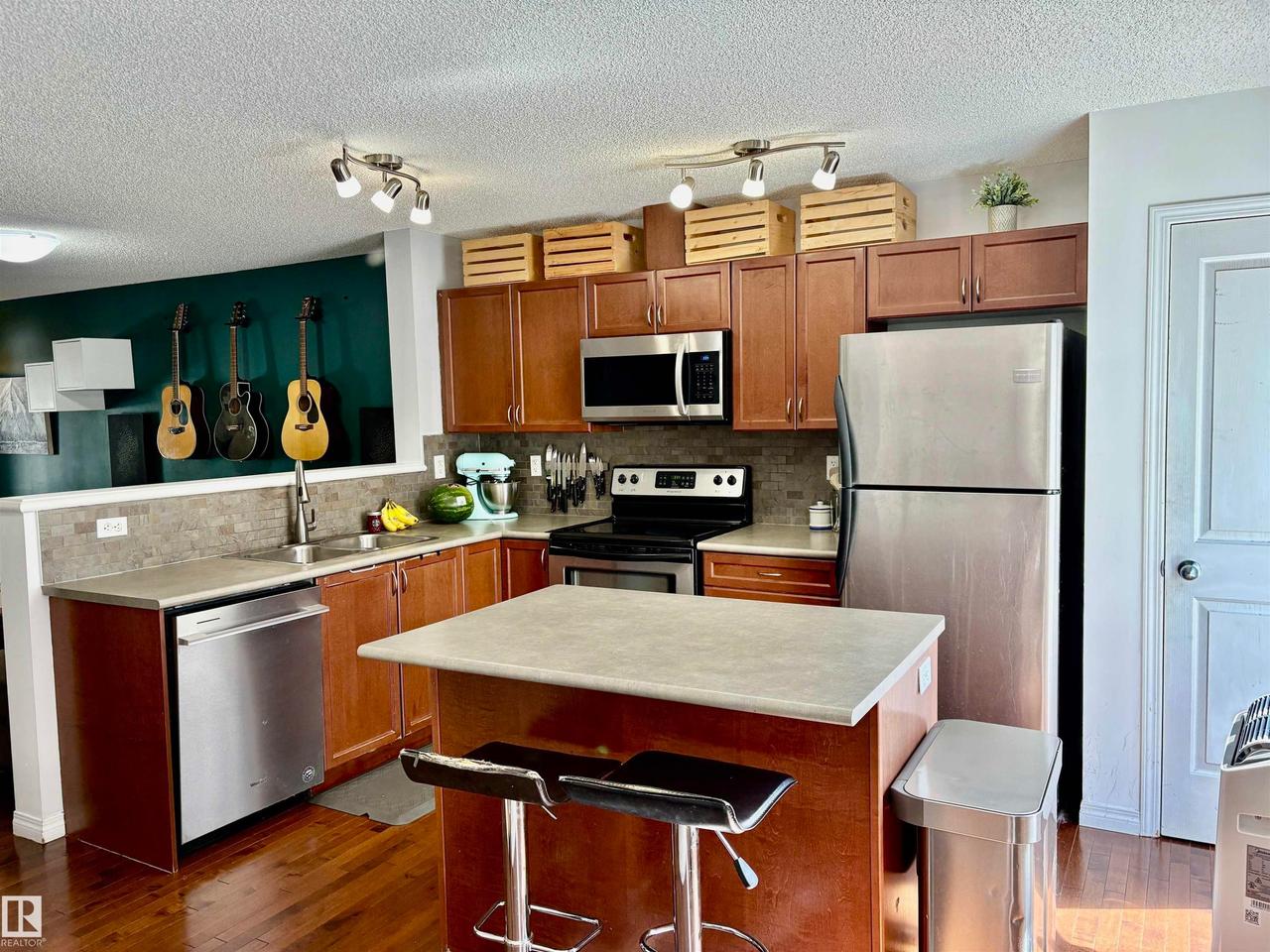 Kitchen featuring wood-finish cabinetry, stainless steel appliances, and a central island with a breakfast bar - #184 1804 70 St Sw, Edmonton, AB - Indoor Photo Showing Kitchen With Double Sink