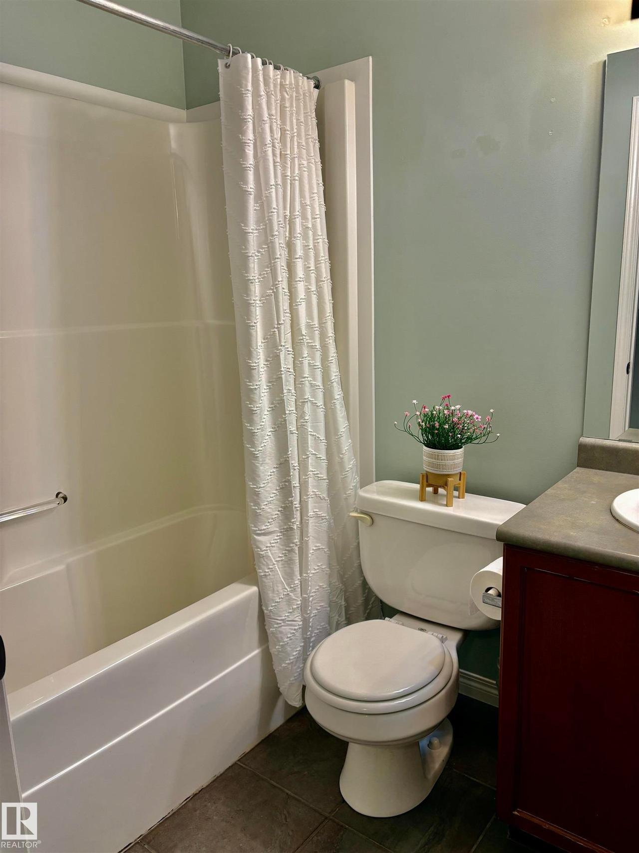 Bathroom featuring a white tub/shower combination with a grab bar, a white toilet, a vanity with a dark countertop, and tile flooring - #184 1804 70 St Sw, Edmonton, AB - Indoor Photo Showing Bathroom