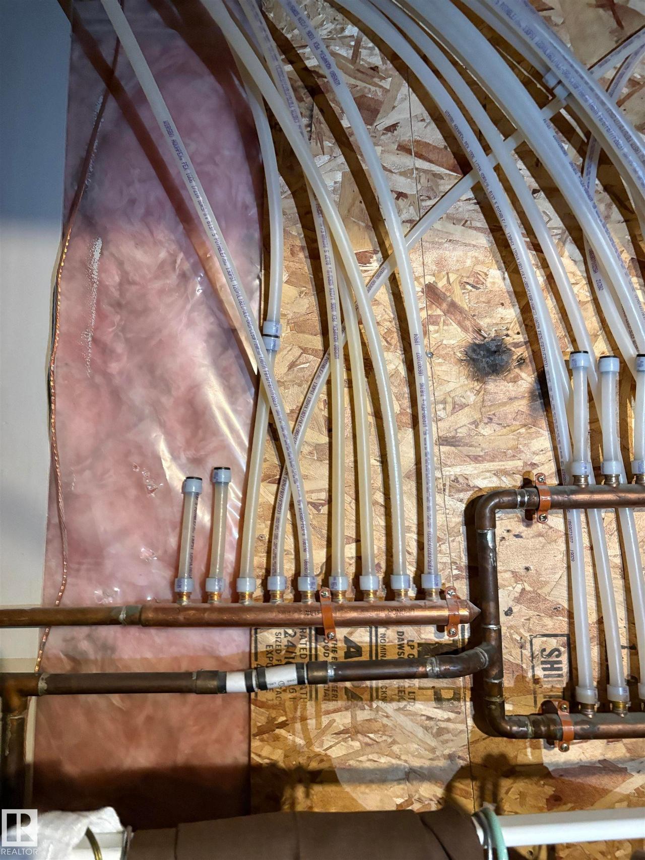 PEX tubing and copper piping system mounted on plywood sheathing, with visible insulation in the background - #184 1804 70 St Sw, Edmonton, AB -  Photo Showing Other Room