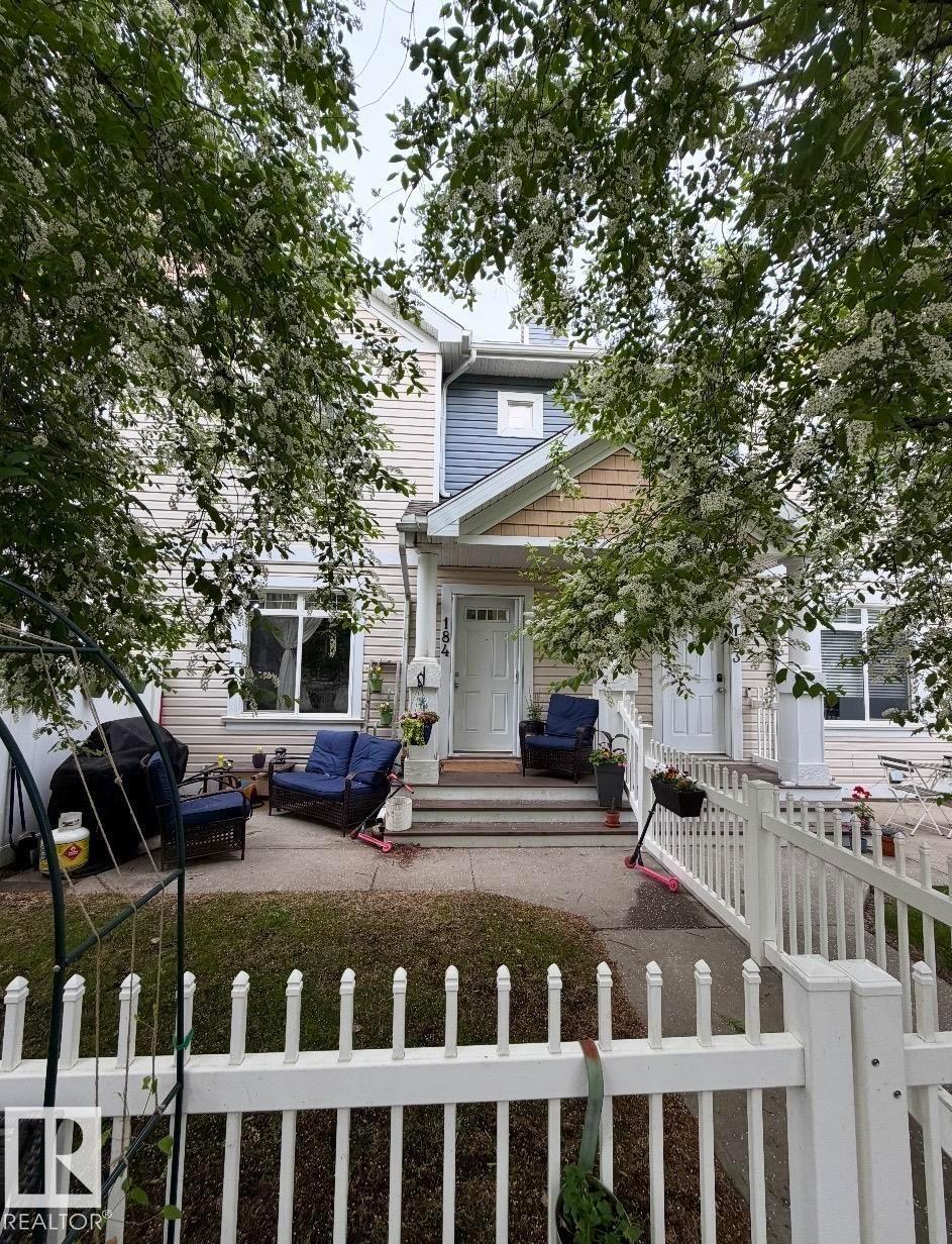 Cream siding exterior with a light blue upper accent, gabled entryways, and a white picket fence - #184 1804 70 St Sw, Edmonton, AB - Outdoor With Facade