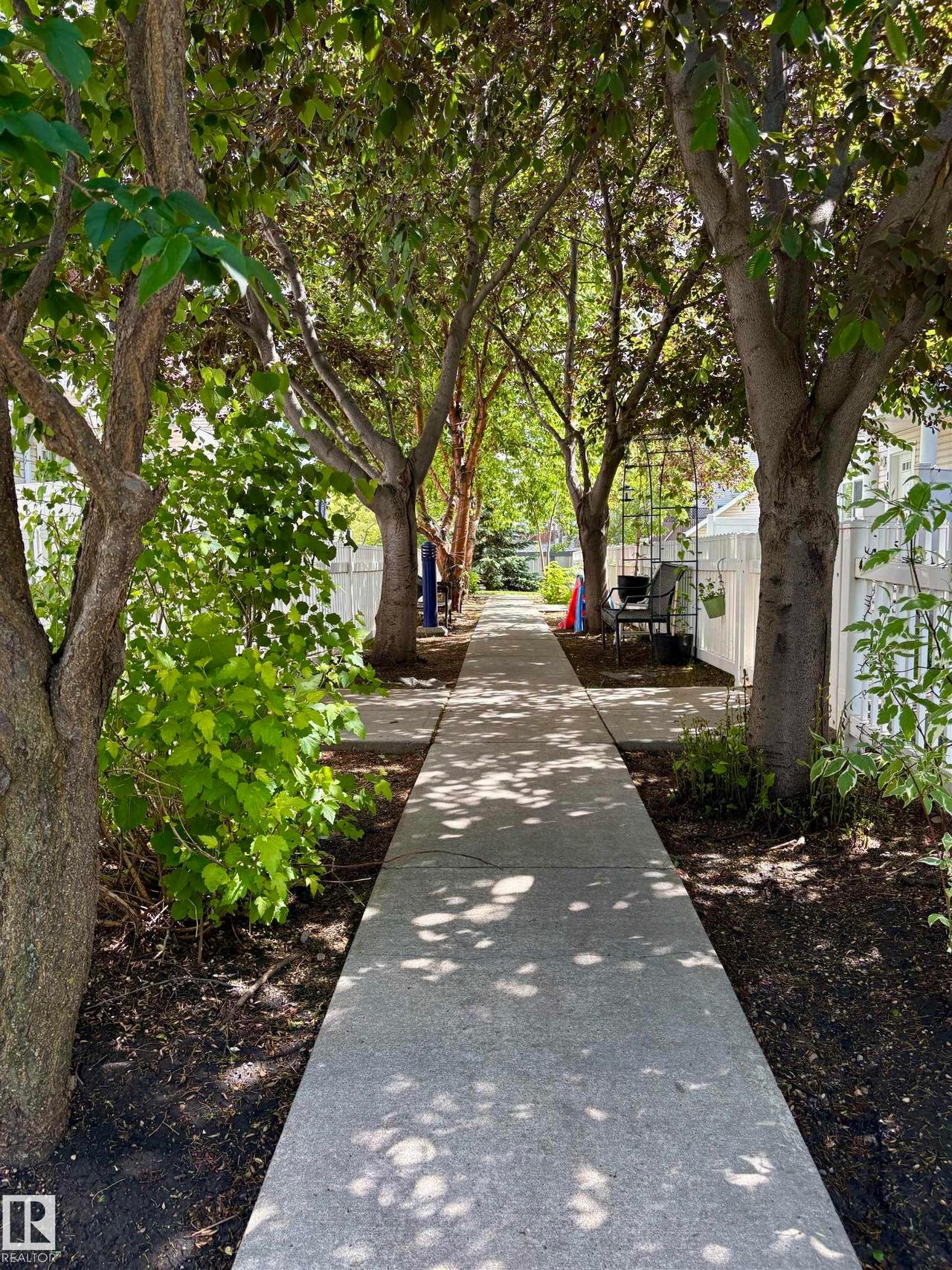 Concrete pathway bordered by mature trees and lush greenery - #184 1804 70 St Sw, Edmonton, AB - Outdoor