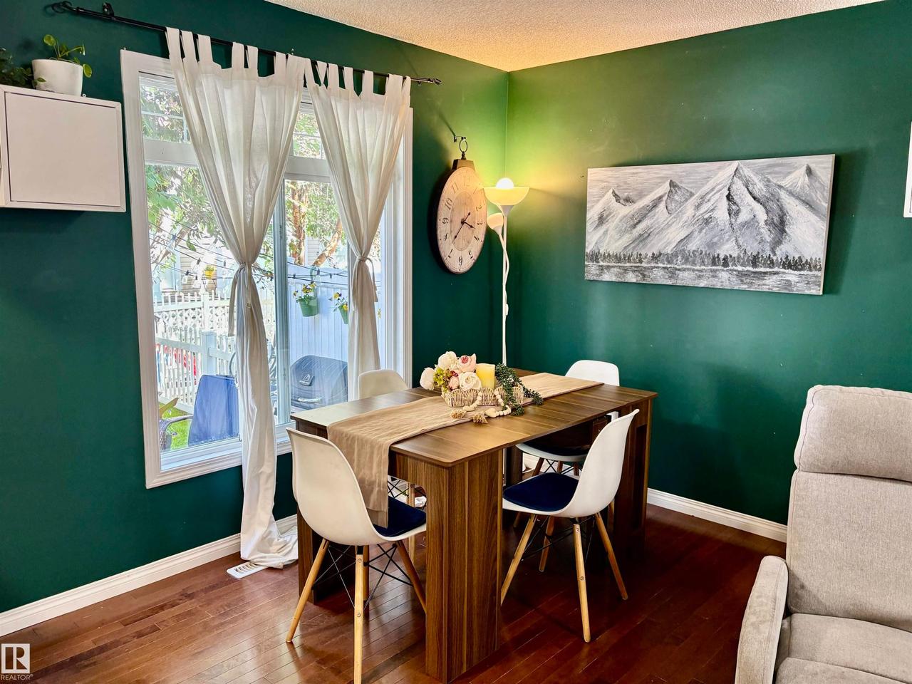 Dining area featuring deep green walls, a large window, rich wood-finish flooring, and white baseboards - #184 1804 70 St Sw, Edmonton, AB - Indoor Photo Showing Dining Room