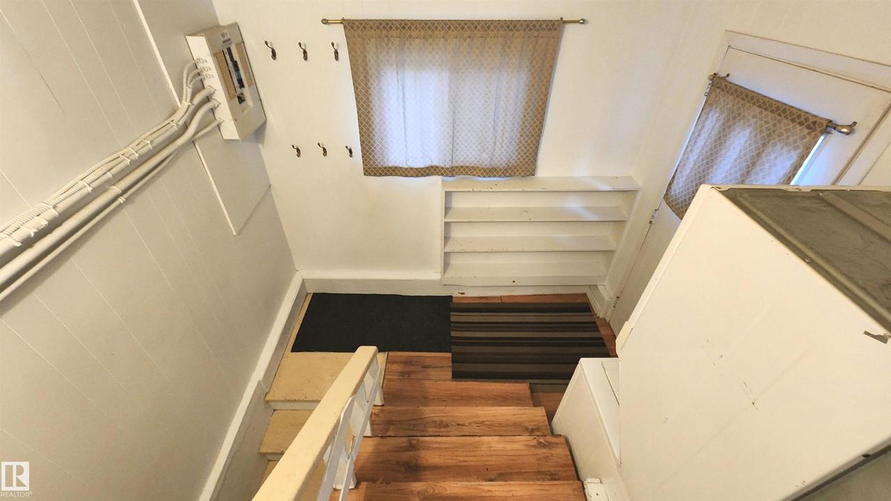 Wood-finish stairs leading to a landing with built-in shelving and two windows - 9359 92 Street Nw, Edmonton, AB - Indoor Photo Showing Other Room