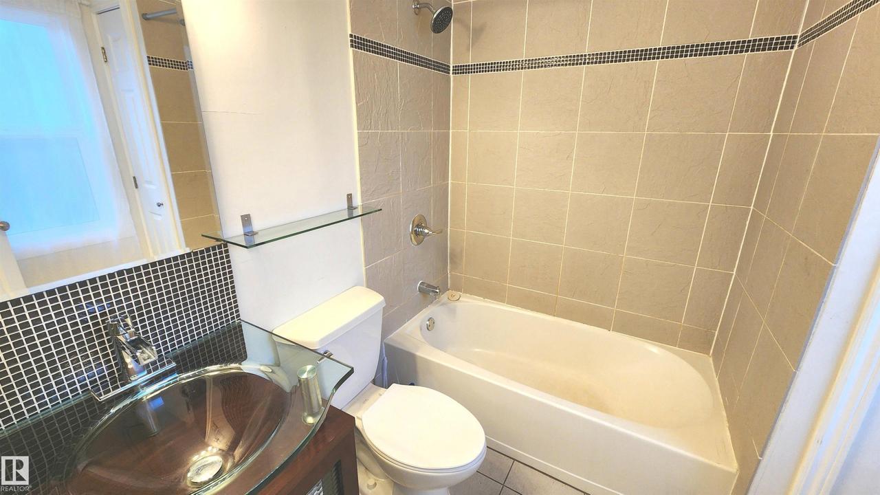 Bathroom featuring a glass vessel sink, dark wood-finish vanity, and black mosaic tile backsplash - 9359 92 Street Nw, Edmonton, AB - Indoor Photo Showing Bathroom