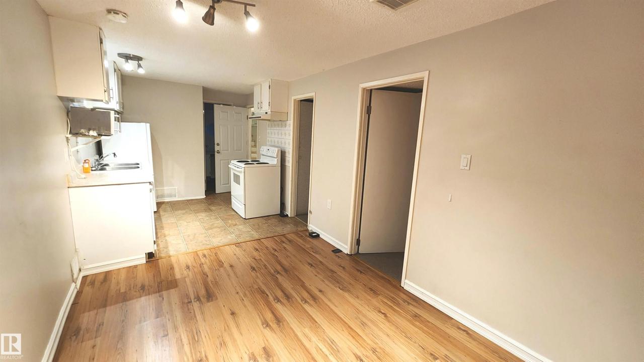 Kitchen and dining area featuring wood-finish flooring, light gray wall paint, white cabinetry, track lighting, and a white appliance package - 9359 92 Street Nw, Edmonton, AB - Indoor Photo Showing Kitchen