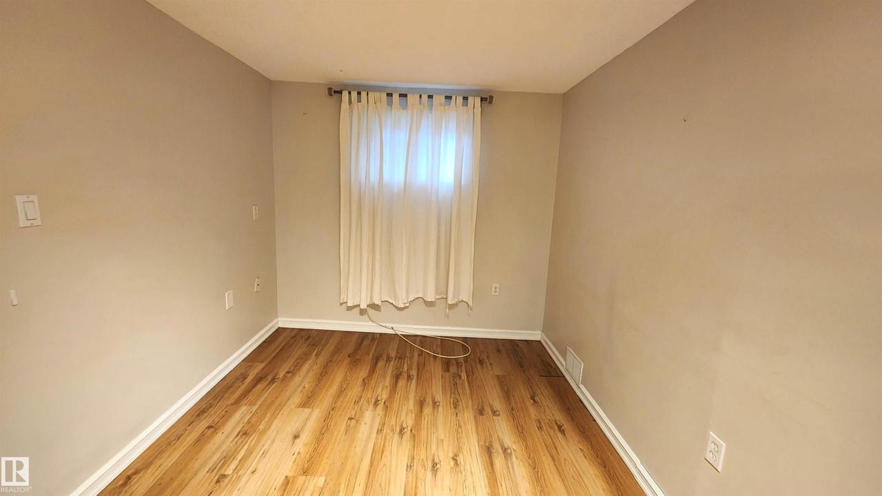 Room featuring wood-finish flooring, light tan walls, and white baseboards - 9359 92 Street Nw, Edmonton, AB - Indoor Photo Showing Other Room