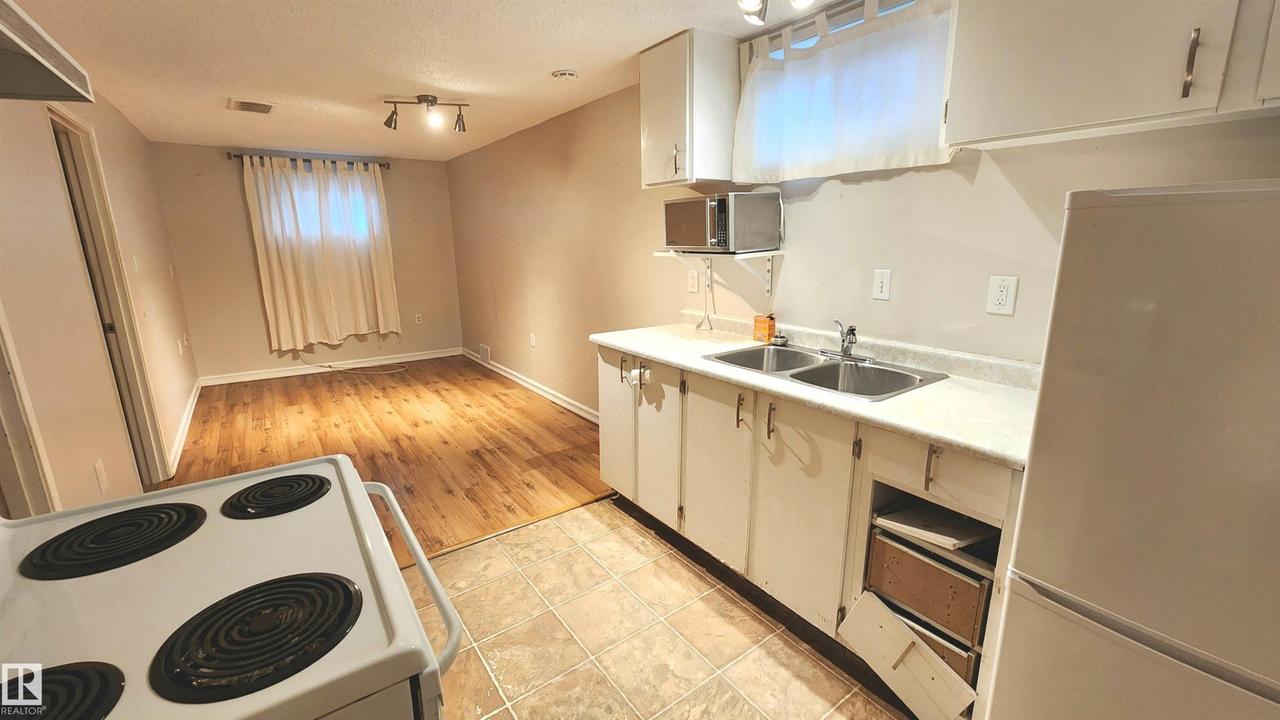 Compact kitchen area featuring a double basin sink, white cabinetry, and a refrigerator - 9359 92 Street Nw, Edmonton, AB - Indoor Photo Showing Kitchen With Double Sink