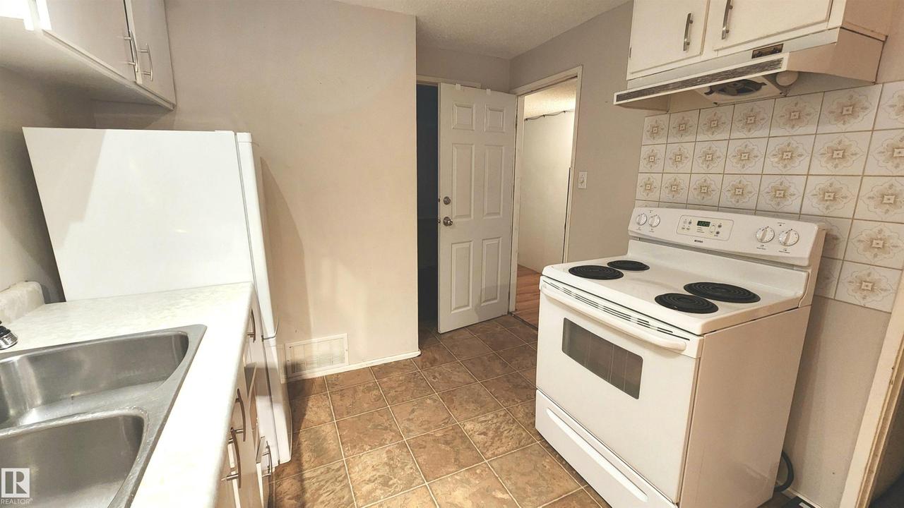 Kitchen featuring tiled flooring, white cabinetry, a double basin stainless steel sink, and a patterned tile backsplash - 9359 92 Street Nw, Edmonton, AB - Indoor Photo Showing Kitchen