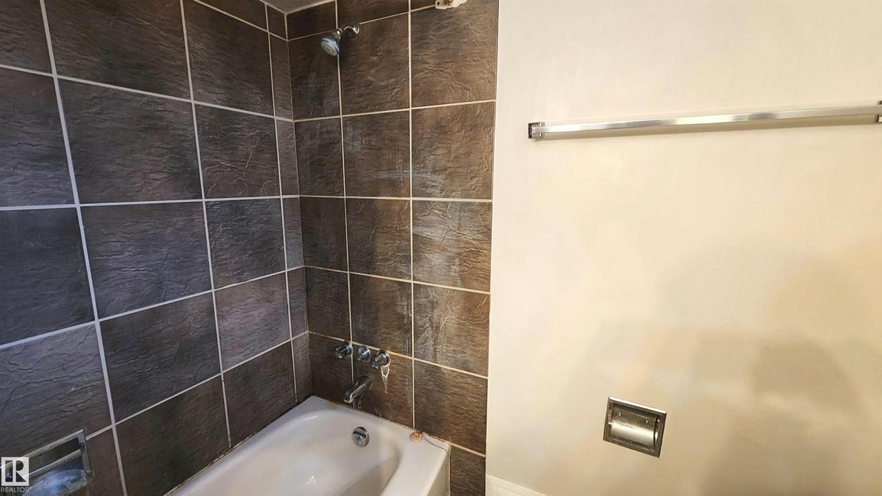 Bathtub with dark-toned wall tiling, coordinating shower head, and chrome fixtures - 9359 92 Street Nw, Edmonton, AB - Indoor Photo Showing Bathroom