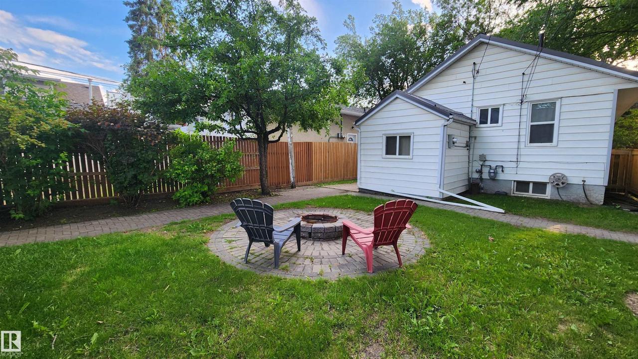 Manicured lawn featuring a circular paver patio with a built-in fire pit - 9359 92 Street Nw, Edmonton, AB - Outdoor