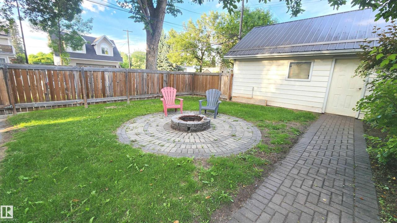 Backyard featuring a circular paver fire pit area, manicured lawn, and a full wood privacy fence - 9359 92 Street Nw, Edmonton, AB - Outdoor