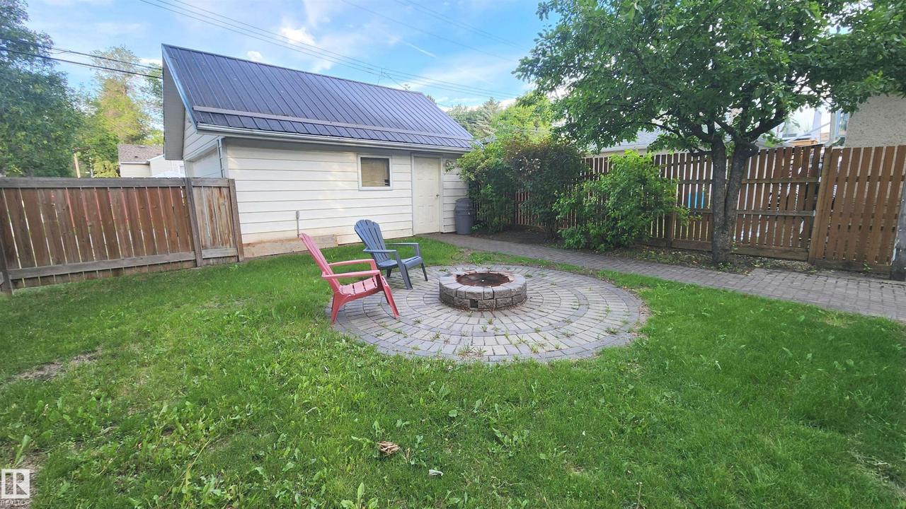 Spacious backyard featuring a circular paver patio with a built-in stone fire pit, a detached garage with a dark metal roof, and a privacy fence - 9359 92 Street Nw, Edmonton, AB - Outdoor
