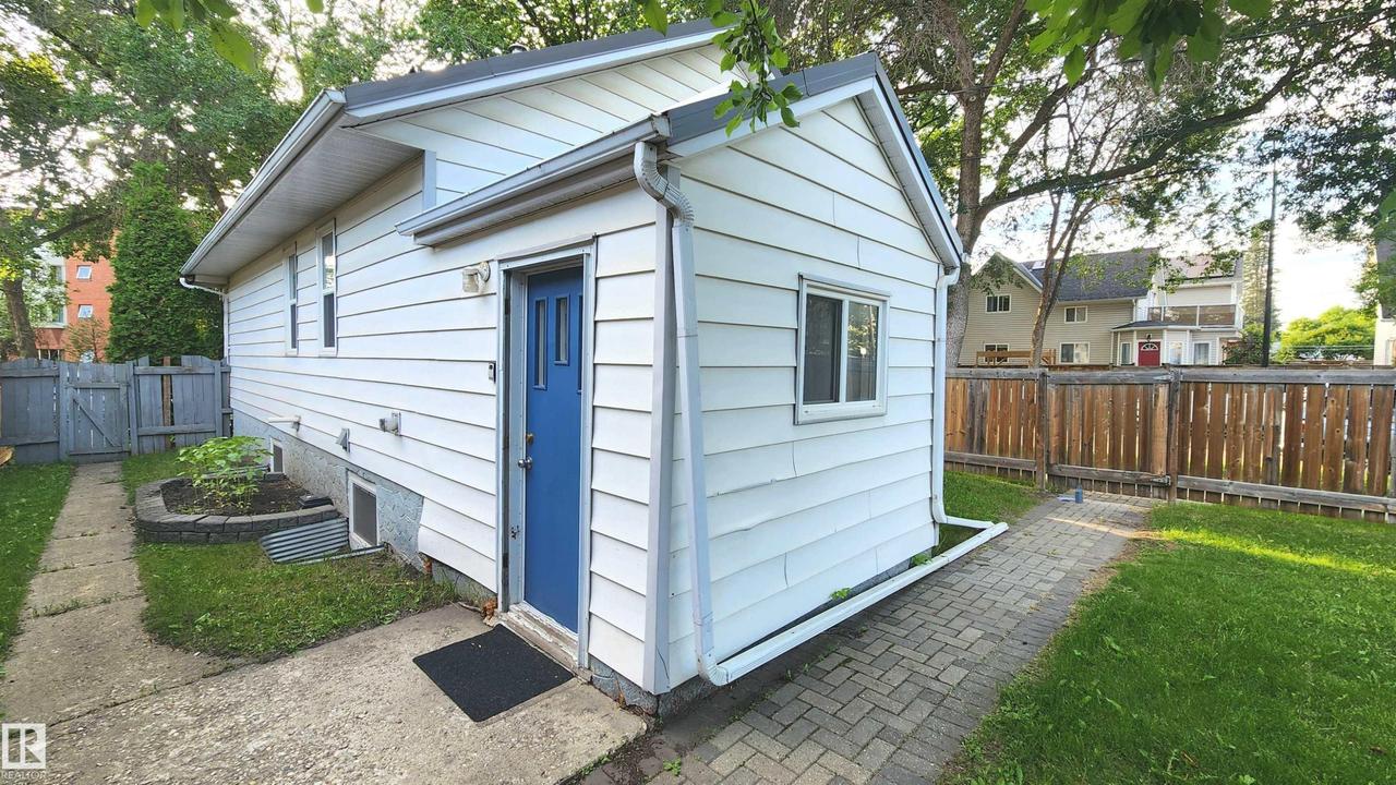 White siding exterior with a vibrant blue entrance door, multiple windows, and a paved walkway - 9359 92 Street Nw, Edmonton, AB - Outdoor With Exterior
