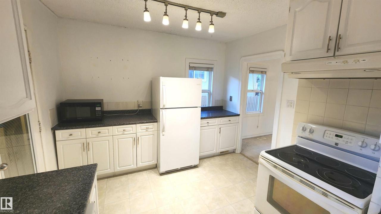 Kitchen featuring white cabinetry, dark countertops, a white electric range with overhead ventilation, and track lighting - 9359 92 Street Nw, Edmonton, AB - Indoor Photo Showing Kitchen