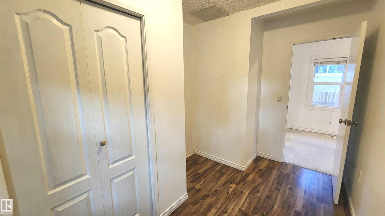 Interior hallway featuring wood-finish flooring, white baseboards, and a paneled bifold closet door with a brass knob - 9359 92 Street Nw, Edmonton, AB - Indoor Photo Showing Other Room