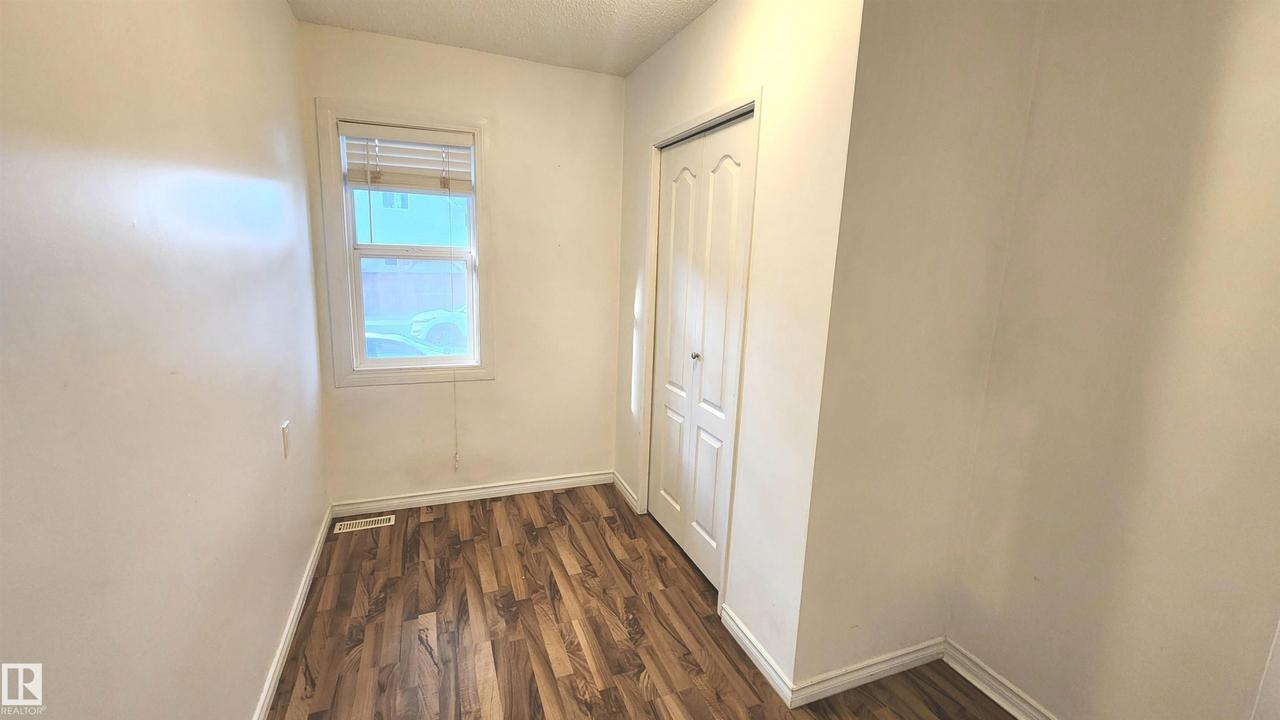 Room featuring wood-finish flooring, white baseboards, a single window with horizontal blinds, and a white bi-fold closet door - 9359 92 Street Nw, Edmonton, AB - Indoor Photo Showing Other Room