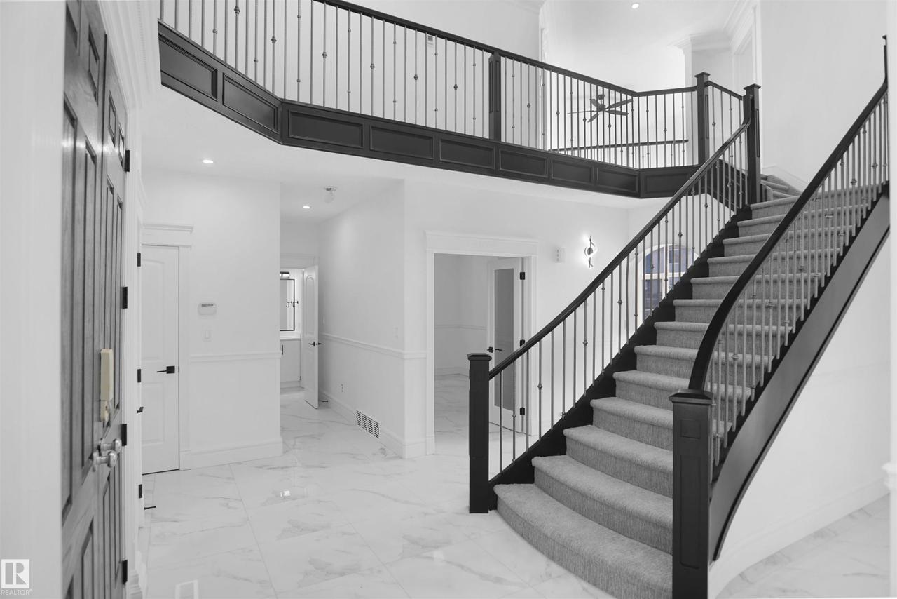 Two-story foyer featuring an elegant curved staircase with carpeted treads, dark wood newel posts, and wrought iron balusters - 6823 18 Avenue Sw, Edmonton, AB - Indoor Photo Showing Other Room