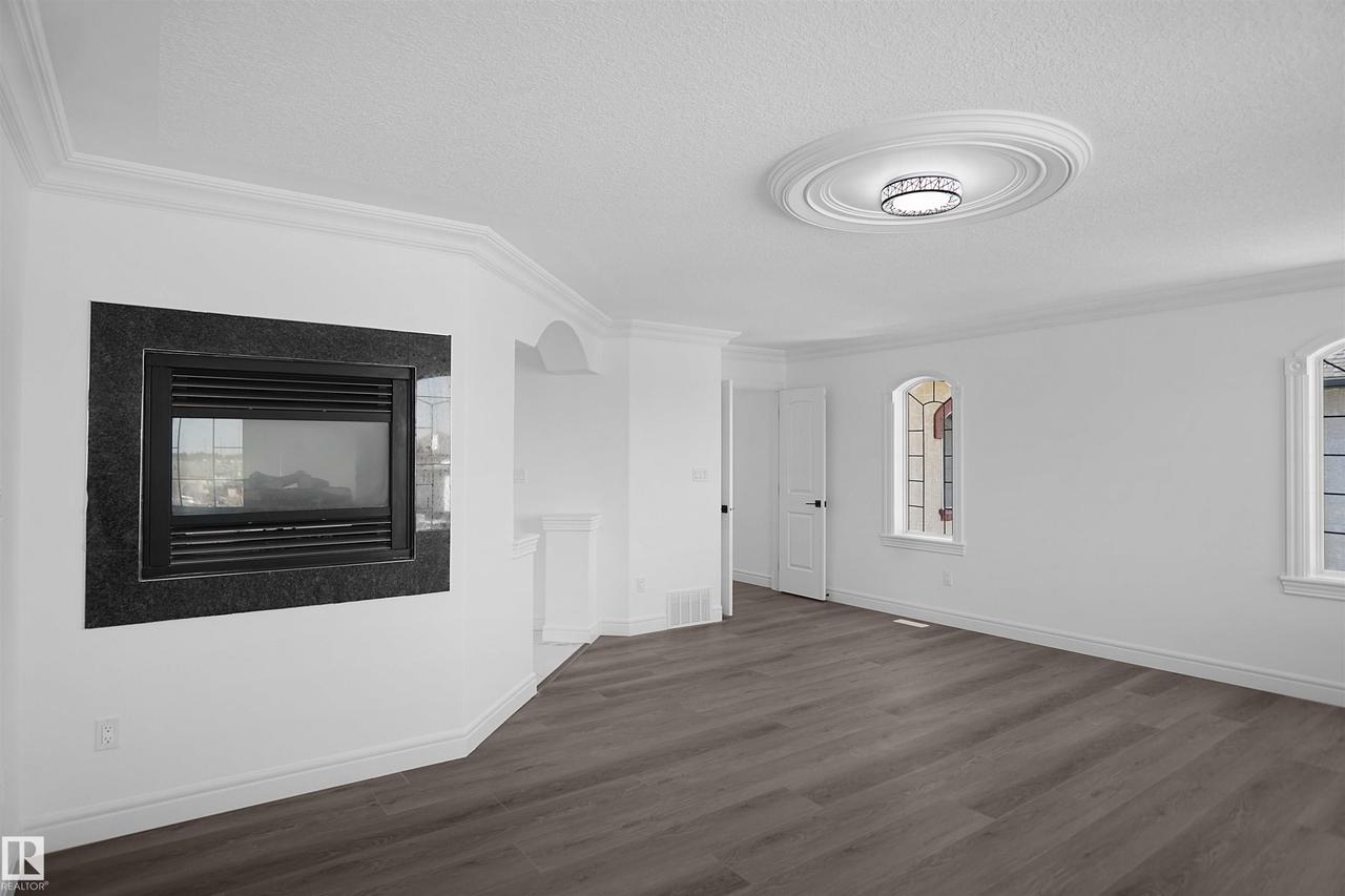 Recessed fireplace with a dark stone surround, crown molding, a decorative ceiling medallion, flush-mount lighting, and wood-finish flooring - 6823 18 Avenue Sw, Edmonton, AB - Indoor With Fireplace