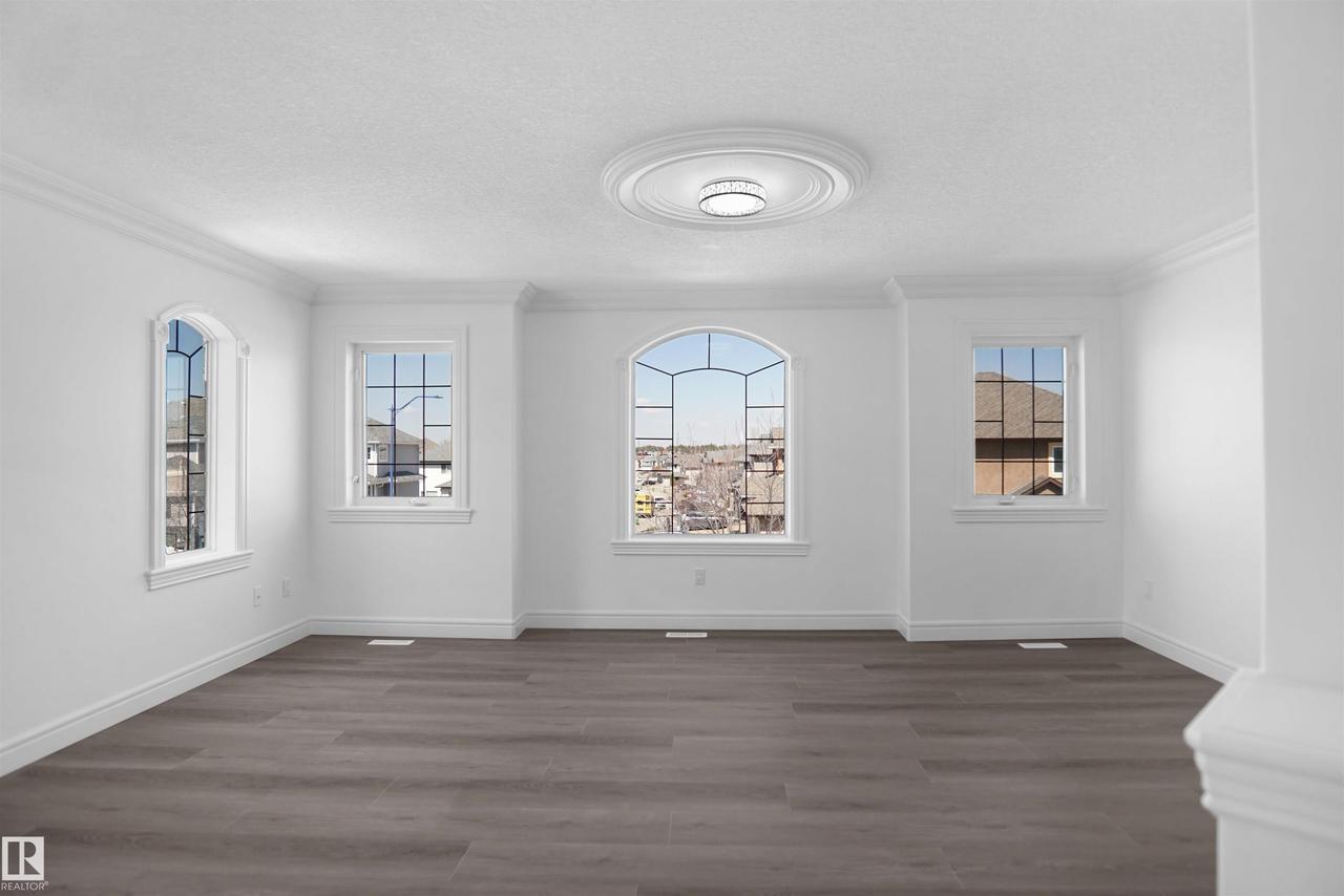 Spacious room featuring wood-finish flooring, a decorative ceiling medallion with an attached light fixture, crown molding, and multiple windows including an arched window - 6823 18 Avenue Sw, Edmonton, AB - Indoor Photo Showing Other Room