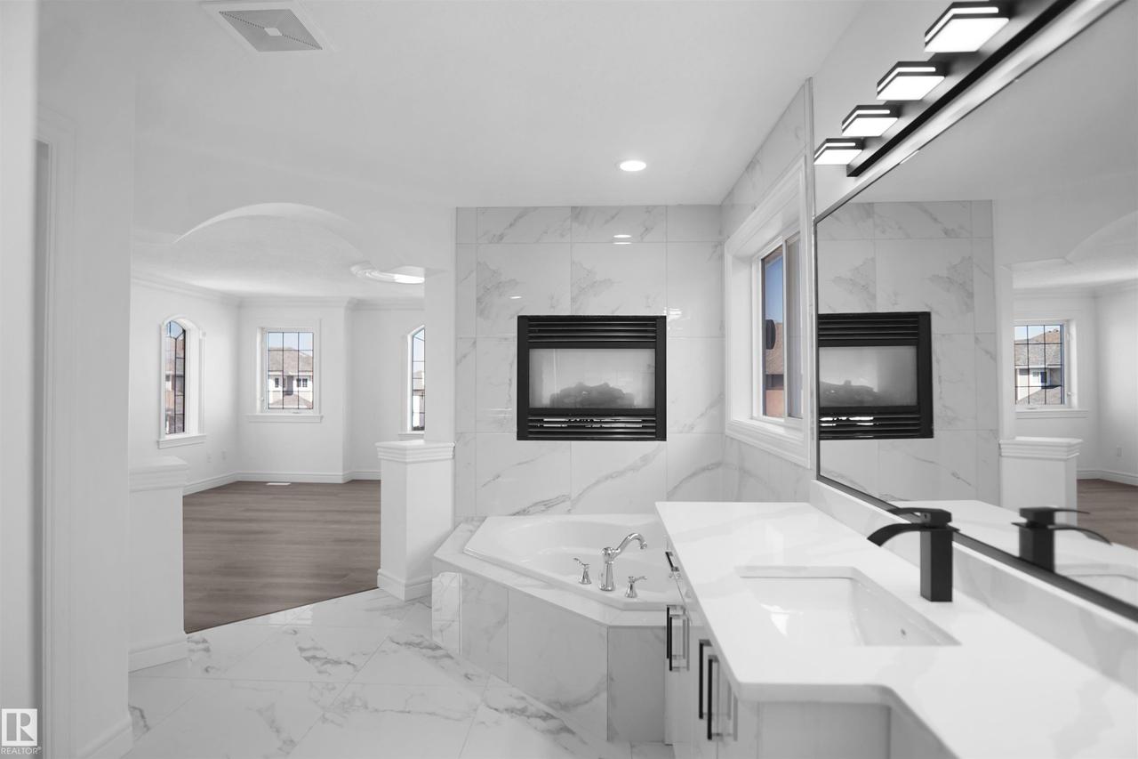 Soaking tub with tile surround, built-in fireplace, vanity with integrated sink, matte black faucet, and large mirror with integrated lighting - 6823 18 Avenue Sw, Edmonton, AB - Indoor Photo Showing Other Room With Fireplace