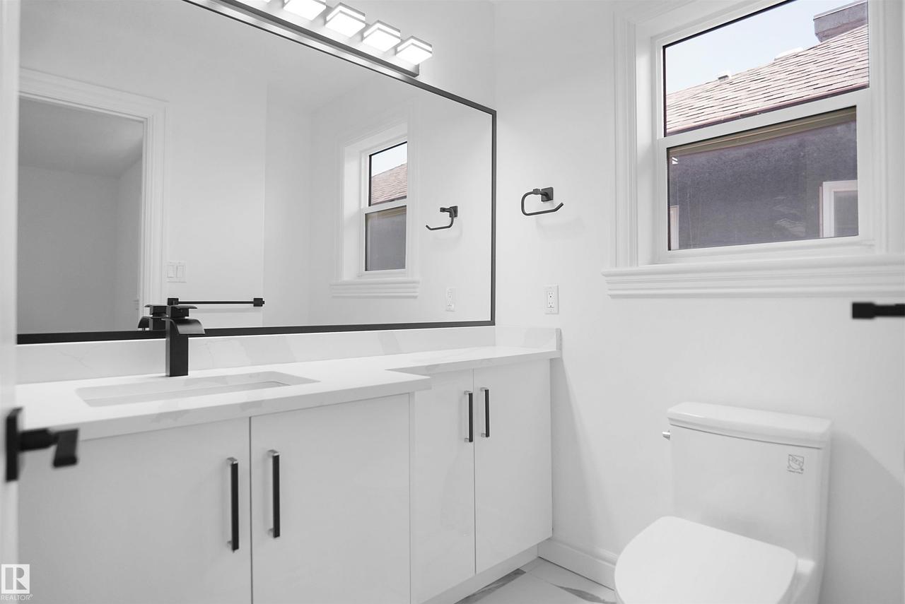 White vanity with flat panel cabinetry, black hardware, and a white countertop with an integrated sink - 6823 18 Avenue Sw, Edmonton, AB - Indoor Photo Showing Bathroom