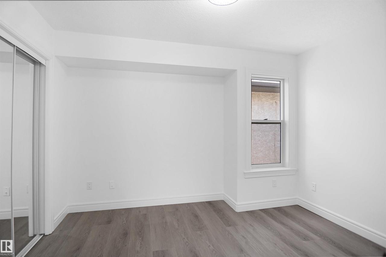 Recessed wall alcove, wood-finish flooring, single window, mirrored closet doors, and a flush-mount ceiling light fixture - 6823 18 Avenue Sw, Edmonton, AB - Indoor Photo Showing Other Room