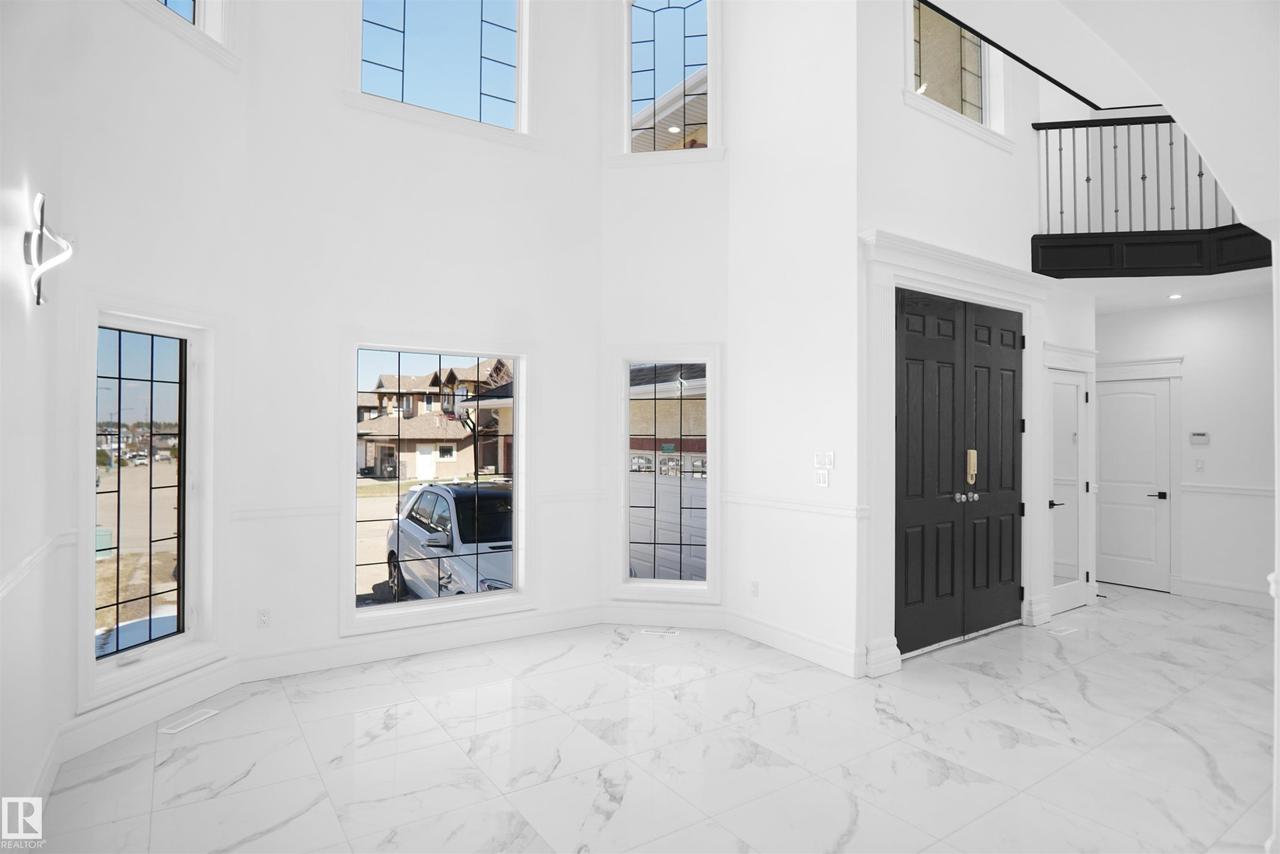 Two-story foyer featuring a double-height ceiling, large grid-pattern windows, marble-pattern flooring, and a dark double entry door with gold-tone hardware - 6823 18 Avenue Sw, Edmonton, AB -  Photo Showing Other Room